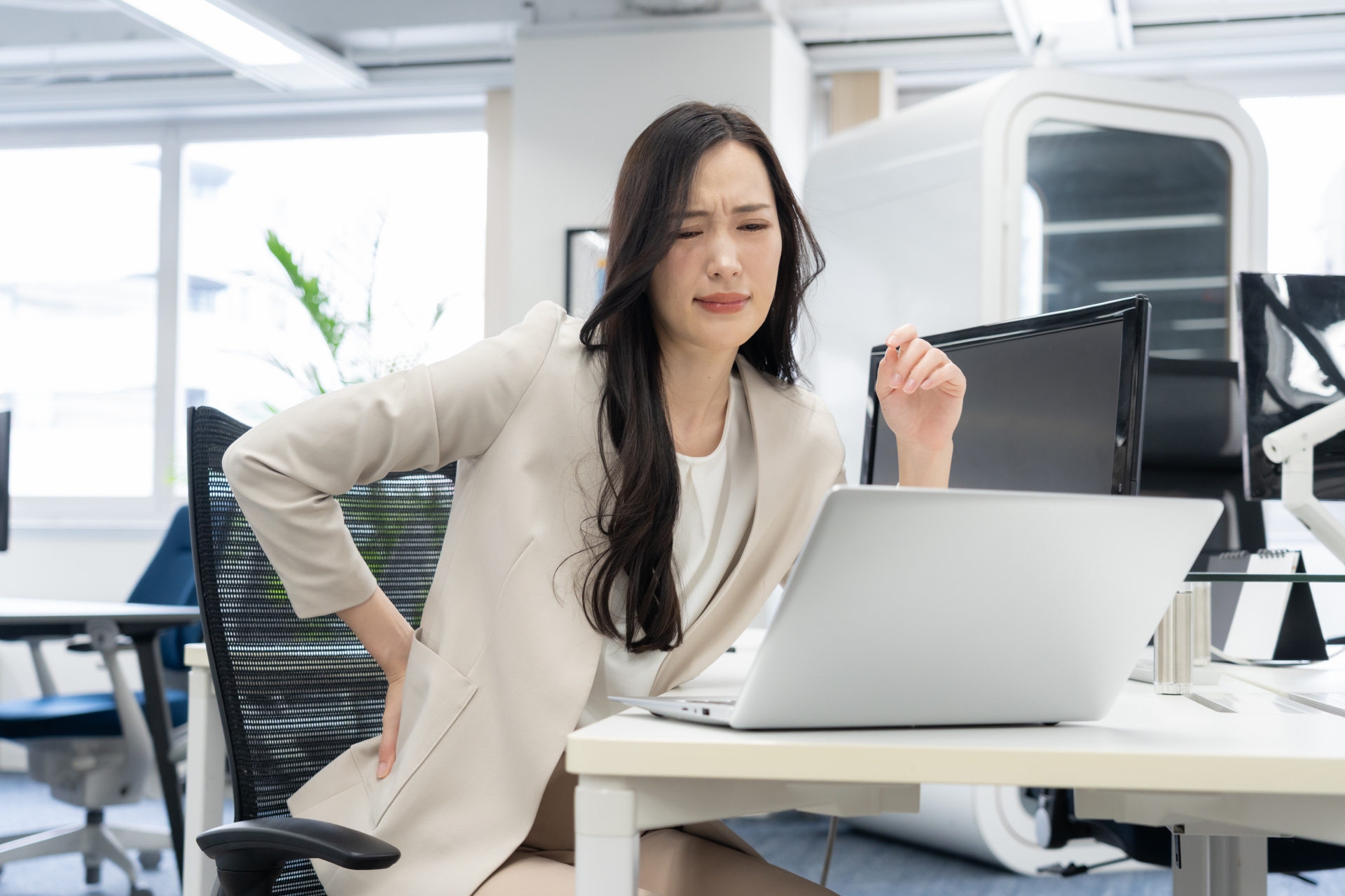 オフィスワークで腰痛に悩む女性の画像